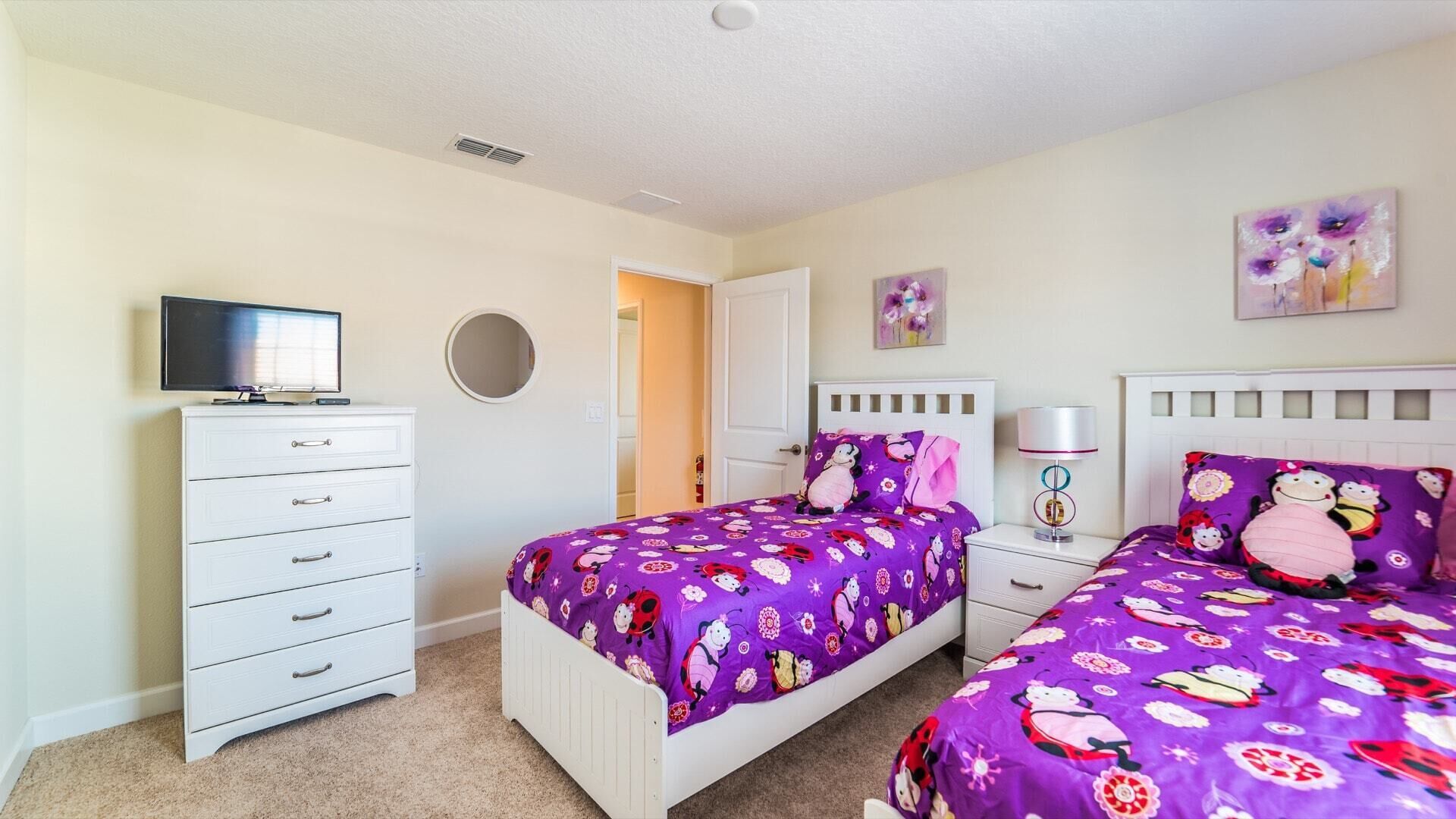 A bedroom with two beds, a TV on a dresser, and a door leading to another room.