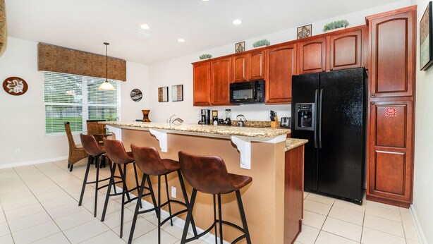 A kitchen with a central island, bar stools, wooden cabinets, a black refrigerator, and a microwave. - Grh9249ha - Windsor Hills Resort - 4 Bed 4 Baths Villa (Kissimmee)