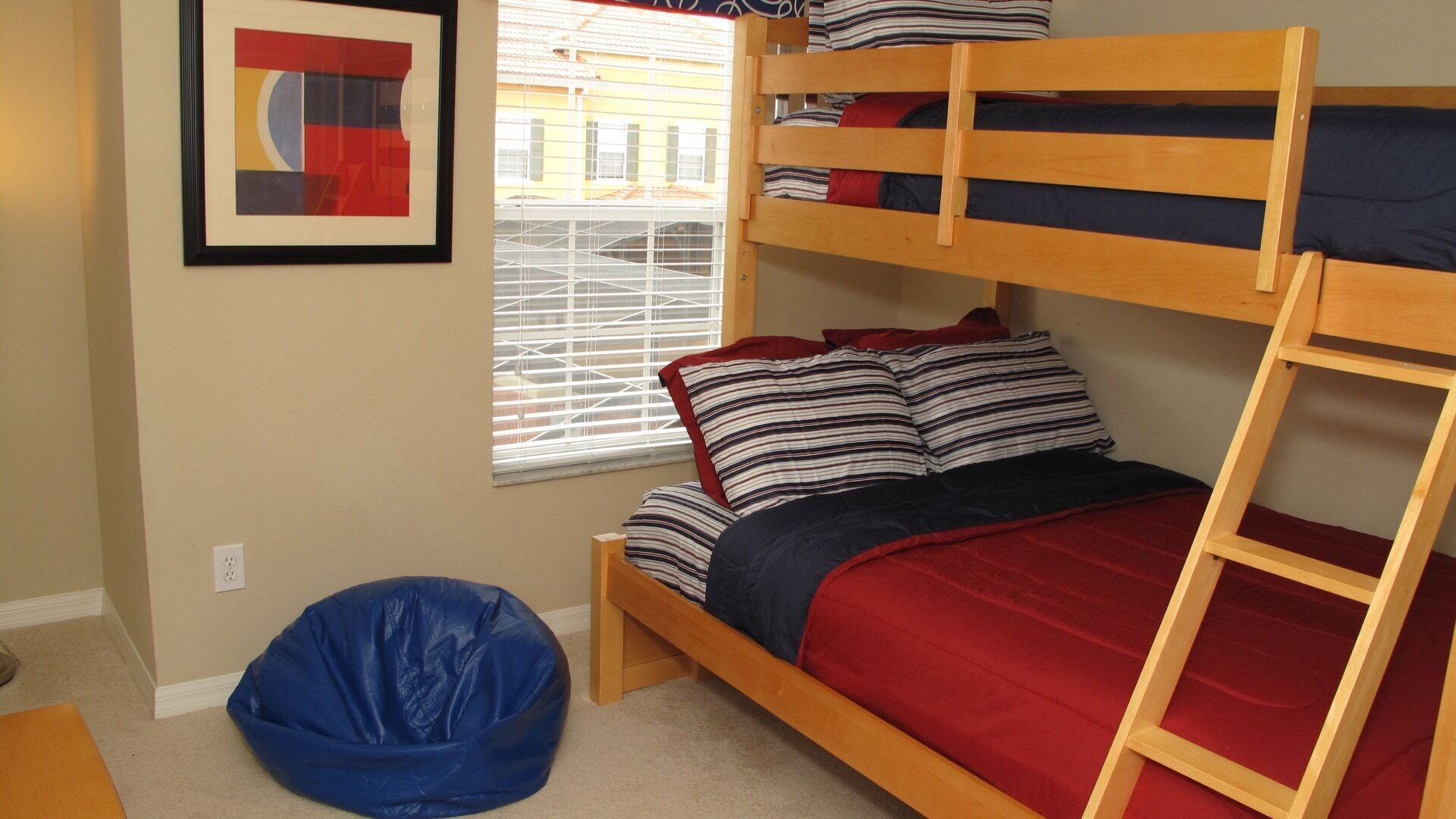 A bunk bed with striped pillows, a blue bean bag, and a framed abstract painting on the wall.