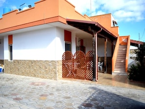 Une maison à deux étages dotée d’un porche couvert, d’un mur en pierre et d’une terrasse carrelée.