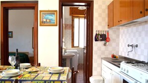 A compact kitchen with a dining area, featuring a tiled backsplash, wooden cabinets, a stove, and a sink. - Tanoshii Holiday Home on the Ground Floor With Outdoor Space and Parking Space (Melendugno)