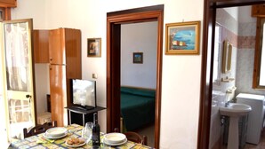 A dining area with a table set for four, a television, and a mirror reflecting a bedroom with a bed and a painting. - Tanoshii Holiday Home on the Ground Floor With Outdoor Space and Parking Space (Melendugno)