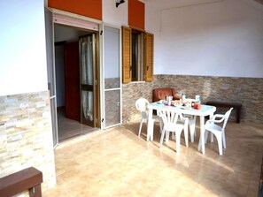 Un espace extérieur aménagé pour les repas, avec une table et des chaises, un banc et un mur en pierre.