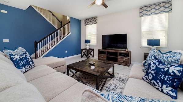 A living room with a staircase, a flat-screen TV, and a coffee table. - Grh9284ha - Solara Resort - 6 Bed 4 Baths Villa (Kissimmee)