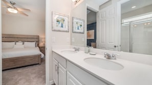 A bedroom with a bed, a ceiling fan, and a bathroom with a large mirror, two sinks, and cabinets. - Grh9285ha - Solara Resort - 7 Bed 6.5 Baths Villa (Kissimmee)