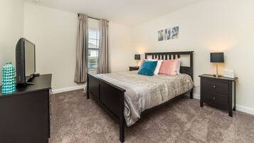 A bedroom with a bed, a nightstand, a dresser, a window with curtains, and a wall with artwork.
