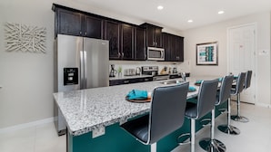 A modern kitchen with dark cabinets, a granite countertop, and bar stools. - Grh9317ha - Solara Resort - 6 Bed 4 Baths Villa (Kissimmee)