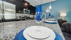 A kitchen with dark cabinets, a microwave, and a sink. There is a dining area with a table set for two, featuring white plates and blue placemats.