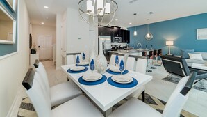 A modern dining area with a white table set for four, a kitchen in the background, and a blue accent wall.