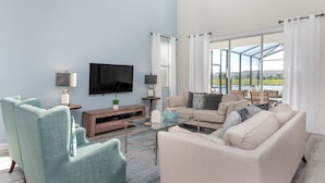 A modern living room with a flat-screen TV, two armchairs, a sofa, and a glass coffee table. - Grh9342ha - Storey Lake Resort - 5 Bed 5 Baths Villa (Kissimmee)