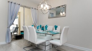 A modern dining area with a glass table, white chairs, and decorative blue vases. - Grh9346ha - Storey Lake Resort - 4 Bed 3 Baths Townhome (Kissimmee)