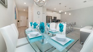 A modern dining area with a glass table set for four, white chairs, and teal napkin holders. - Grh9346ha - Storey Lake Resort - 4 Bed 3 Baths Townhome (Kissimmee)