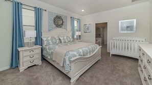 A bedroom with a large bed, a nightstand, a dresser, a crib, and a bathroom door. - Grh9354ha - Windsor At Westside Resort - 9 Bed 6 Baths Villa (Kissimmee)