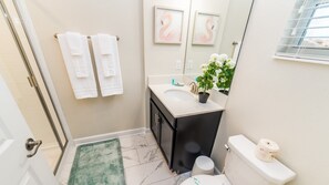 A bathroom with a white sink, dark cabinet, and a toilet. There are two white towels hanging on a rack, a green rug, and a potted plant on the sink. - Grh10325ha - Champions Gate Resort - 5 Bed 4 Baths Townhome (Davenport)