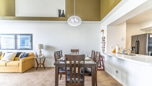 A modern living room with a yellow sofa, a dining table with chairs, and a kitchen area with a refrigerator and sink. - It9921 - 4 Condo in Royal Palm Bay Resort, Sleeps Up To 8, Just 5 Miles To Disney (Kissimmee)