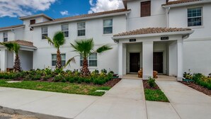 A modern two-story residential building with a white exterior, numbered 1583, featuring a tiled roof, multiple windows, and a well-maintained front garden with palm trees and flowering plants. - Fs10380ha - Champions Gate Resort - 4 Bed 3 Baths Townhouse (Davenport)