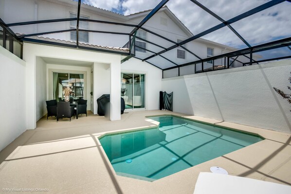 A covered swimming pool with a glass ceiling, a dining area with chairs and a table, and a white exterior wall. - Fs10380ha - Champions Gate Resort - 4 Bed 3 Baths Townhouse (Davenport)