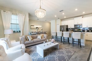 A modern living room with a sofa, coffee table, and bar stools. There is a kitchen area with a refrigerator, microwave, and bar counter. - Fs10380ha - Champions Gate Resort - 4 Bed 3 Baths Townhouse (Davenport)