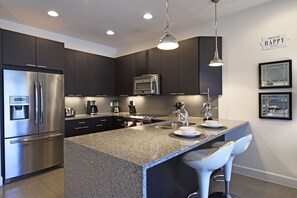 Une cuisine moderne avec des meubles de couleur sombre, des appareils en acier inoxydable, un plan de travail en granit et des tabourets de bar.