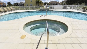 Una piscina con un jacuzzi en el centro, rodeada de sillas de descanso y una cerca blanca.