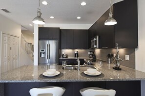 A modern kitchen with dark cabinetry, stainless steel appliances, and granite countertops. - Fs10400ha - Serenity - 3 Bed 3 Baths Townhouse (Clermont)