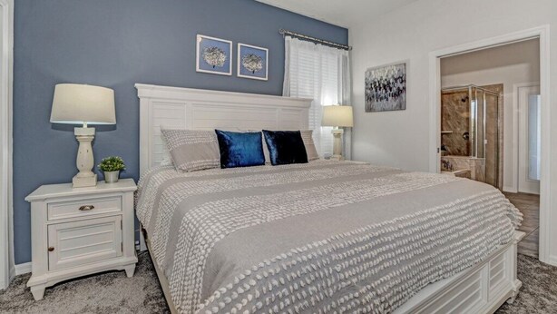 A bedroom with a large bed, two bedside tables with lamps, a white headboard, and artwork on the walls. - Fs10524ha - Windsor At Westside Resort - 7 Bed 6 Baths Villa (Kissimmee)