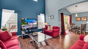 A modern living room with a flat-screen TV, red sofas, a glass coffee table, and a dining area with wooden chairs. - Fs11216ha - Emerald Island Resort - 5 Bed 4 Baths Villa (Kissimmee)