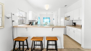 Una cocina con una isla central, armarios blancos y tres taburetes de madera.