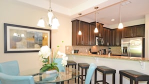 A modern kitchen with dark wood cabinets, stainless steel appliances, and a glass dining table with blue chairs. - Ffv11205ha - Champions Gate Resort - 3 Bed 2.5 Baths Townhome (Davenport)