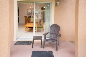A balcony with a chair and a small stool, a sliding glass door leading to an interior room with a table and chairs. - Ihr11308ha - Regal Palms Resort & Spa - 4 Bed 3 Baths Townhouse (Davenport)