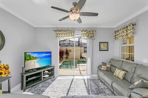 A living room with a television, a grey sofa, patterned rug, and a ceiling fan. - Fs11265ha - Storey Lake Resort - 4 Bed 3 Baths Townhouse (Kissimmee)