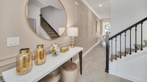 A hallway with a white console table, a round mirror, and a staircase with black railings. - Fs11331ha - Storey Lake Resort - 4 Bed 3 Baths Townhouse (Kissimmee)