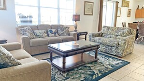 A living room with a sofa, armchair, and coffee table. There are windows with curtains, a lamp, and framed pictures on the wall. - Ffv11368ha - Windwood Bay - 5 Bed 4 Baths Villa (Davenport)