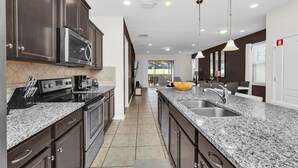 A modern kitchen with dark cabinets, granite countertops, stainless steel appliances, and pendant lighting. - Fs11374ha - Windsor At Westside Resort - 7 Bed 6 Baths Villa (Kissimmee)