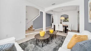 A modern living room with a staircase, white walls, and a dining area with a chandelier. - Fs11371ha - Veranda Palms Resort - 6 Bed 4 Baths Villa (Kissimmee)