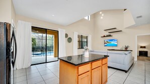 A modern kitchen with a central island, a dining area with a sofa, and a large sliding glass door leading to a balcony. - Fs11379ha - Veranda Palms Resort - 6 Bed 4 Baths Villa (Kissimmee)