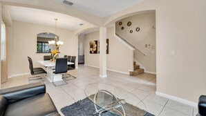 A spacious living room with a glass coffee table, a dining area with a white table and black chairs, and a staircase with a modern design. - Fs11379ha - Veranda Palms Resort - 6 Bed 4 Baths Villa (Kissimmee)