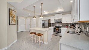 Una cocina moderna con armarios blancos, electrodomésticos de acero inoxidable y una isla central con taburetes.