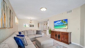 Una sala de estar con un sofá seccional, un reposapiés, un mueble de madera y un televisor de pantalla plana.