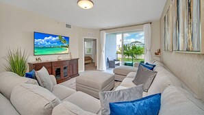 Una sala de estar con un televisor de pantalla plana grande, un sofá color beige y vistas a un balcón con mobiliario exterior.