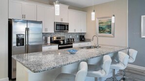 A modern kitchen with white cabinets, stainless steel appliances, granite countertops, and bar seating. - Fs11384ha - Storey Lake Resort - 4 Bed 3 Baths Townhouse (Kissimmee)