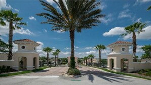 A gated entrance with two small towers, palm trees, and a clear blue sky. - Ffv11387ha - Calabay Parc at Tower Lake - 4 Bed 3 Baths Villa (Haines City)