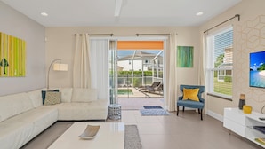 A modern living room with a white sofa, a blue armchair, and a glass door leading to a balcony with a pool. - Fs11372ha - Serenity - 3 Bed 3 Baths Townhouse (Clermont)