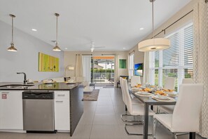 A modern kitchen with a dishwasher, a dining area with a table set for four, and a view of the outdoors through large windows. - Fs11372ha - Serenity - 3 Bed 3 Baths Townhouse (Clermont)