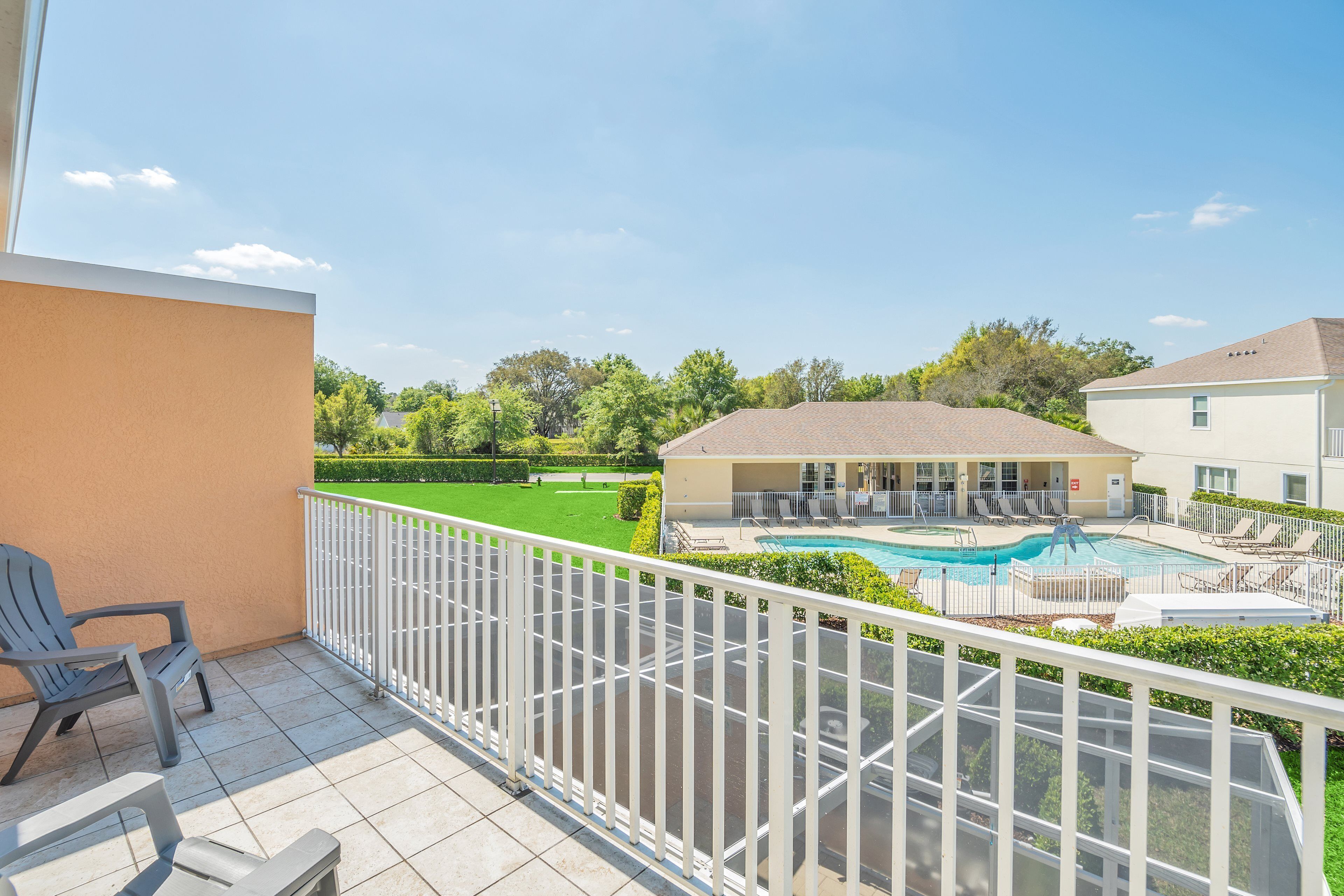 Un balcon avec vue sur une piscine, des chaises longues et une pelouse bien entretenue.