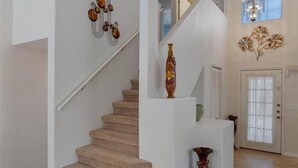 Una escalera con peldaños alfombrados color beige, una pared blanca con un adorno decorativo y una puerta con ventanal.