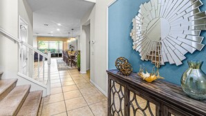 A hallway with a staircase, a decorative mirror, and a console table with a vase and a decorative bowl. - Fs11243ha - Windsor At Westside Resort - 8 Bed 6 Baths Villa (Kissimmee)