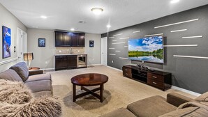 A modern living room with a flat-screen TV, dark wood furniture, and a beige carpet. - Fs11243ha - Windsor At Westside Resort - 8 Bed 6 Baths Villa (Kissimmee)