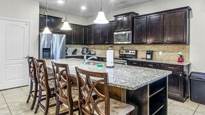 A kitchen with dark wood cabinets, a granite countertop, stainless steel appliances, and wooden chairs. - Fs11243ha - Windsor At Westside Resort - 8 Bed 6 Baths Villa (Kissimmee)