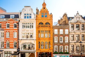 A row of historic buildings with varied architectural styles, including a prominent red brick building with a white facade and a distinctive yellow building with ornate detailing. - Mayfair`s Finest: Modern 2 bedroom apartment! (Greater London)